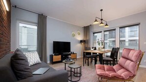A modern living room with a sofa, a pink chair, a TV, a dining table, and a lamp. - Elegant Apartment Near the Old Market Square | Parking (Poznań)