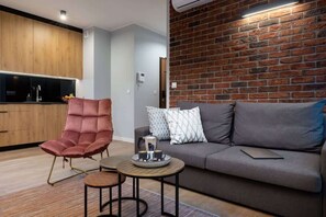 Ein modernes Wohnzimmer mit einem grauen Sofa, einem roten Sessel und einem kleinen runden Tisch mit einer Teeservice und einem Teekessel.