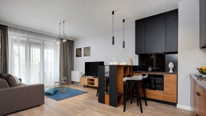 Una sala moderna con un sofá, una mesa de centro y un televisor. Cuenta con una zona de cocina con una mesa y sillas.