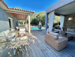 Eine Holzterrasse mit Gartenmöbeln, einem Pool und einer Steinmauer.