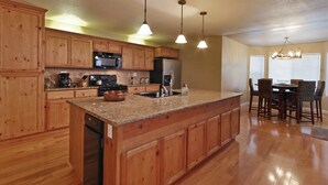A kitchen with wooden cabinets, granite countertops, a built-in dishwasher, a refrigerator, a microwave, and a dining area with a table and chairs. - Comfortable Shaver Lake Getaway (Shaver Lake)