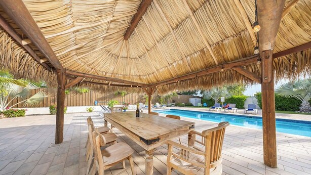 Un espace extérieur abrité, doté d’une piscine, d’une table et de chaises en bois, et d’un toit de chaume.