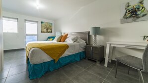 Une chambre à coucher avec un lit, une table de chevet, une chaise et une œuvre d’art accrochée au mur.