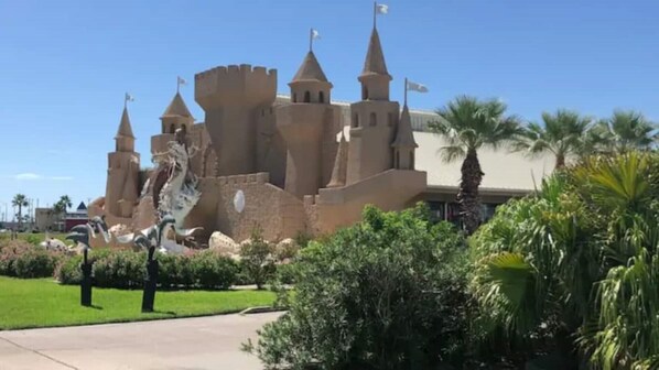 A castle-like building with multiple towers and flags, surrounded by greenery and palm trees.