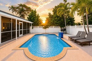 A swimming pool with a white fence, lounge chairs, and a building with large windows. - 6 Bedrooms 4 baths Dream Pool Home near Vanderbilt Beach Naples Florida (Naples)