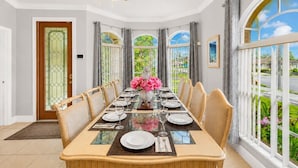 Uma sala de jantar com uma mesa comprida posta para seis pessoas, grandes janelas e um lustre decorativo.