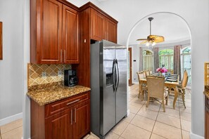 Una cocina con armarios de madera, un refrigerador de acero inoxidable, una cafetera y un comedor con mesa y sillas.