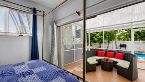 Un dormitorio con cama, puerta corredera de vidrio que da a un patio con mobiliario exterior y piscina.