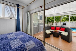 Ein Schlafzimmer mit einem Bett, einer Schiebetür zu einer Terrasse mit Sitzgelegenheit und einem Pool.