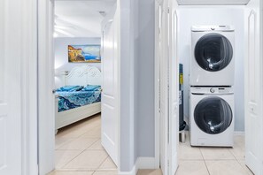 A room with a bed, a painting, and two stacked washing machines.