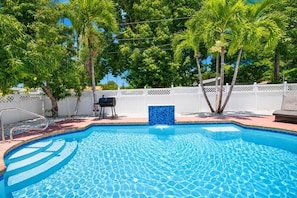 Una piscina con cerco blanco, palmeras y una parrilla.