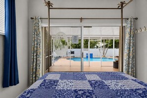 Un dormitorio con cama, vista a una piscina y balcón con cerca blanca.