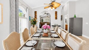 Comedor con una larga mesa dispuesta para seis comensales, un ventilador de techo y un refrigerador al fondo.