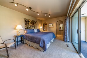 A bedroom with a large bed, two bedside tables with lamps, a chair, a tapestry, and a view through a glass door. - Wapato Point Halmalka Condo 512B Sleeps 8 by Outdoor Pool, Sandy Beach Amenities (Manson)