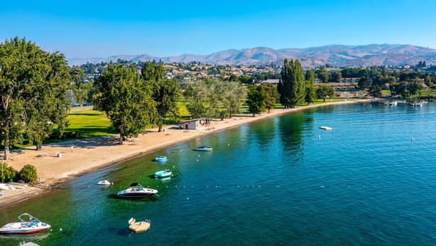 Vista de un lago con barcos, una playa de arena y un parque con árboles.