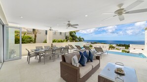 Une terrasse extérieure ensoleillée avec une piscine, un espace salon et une vue sur l’océan.