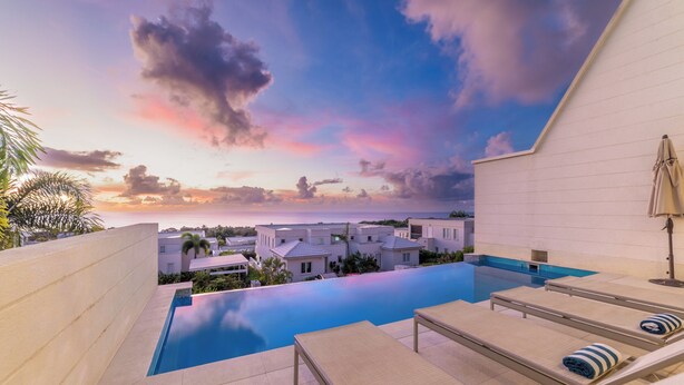 Un espace piscine moderne, doté de chaises longues et offrant une vue sur la mer et les bâtiments en arrière-plan.