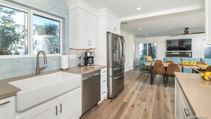 A modern kitchen with white cabinets, stainless steel appliances, and a large window. - Seas the Day on the Bay (San Diego)