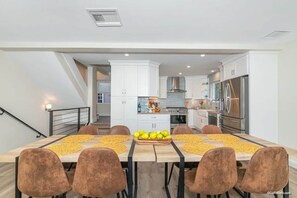 A modern kitchen with white cabinets, stainless steel appliances, and a dining area with a wooden table and brown chairs.