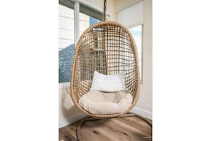 Relax in a hanging chair with a cushion and pillow, suspended from the ceiling near a window.