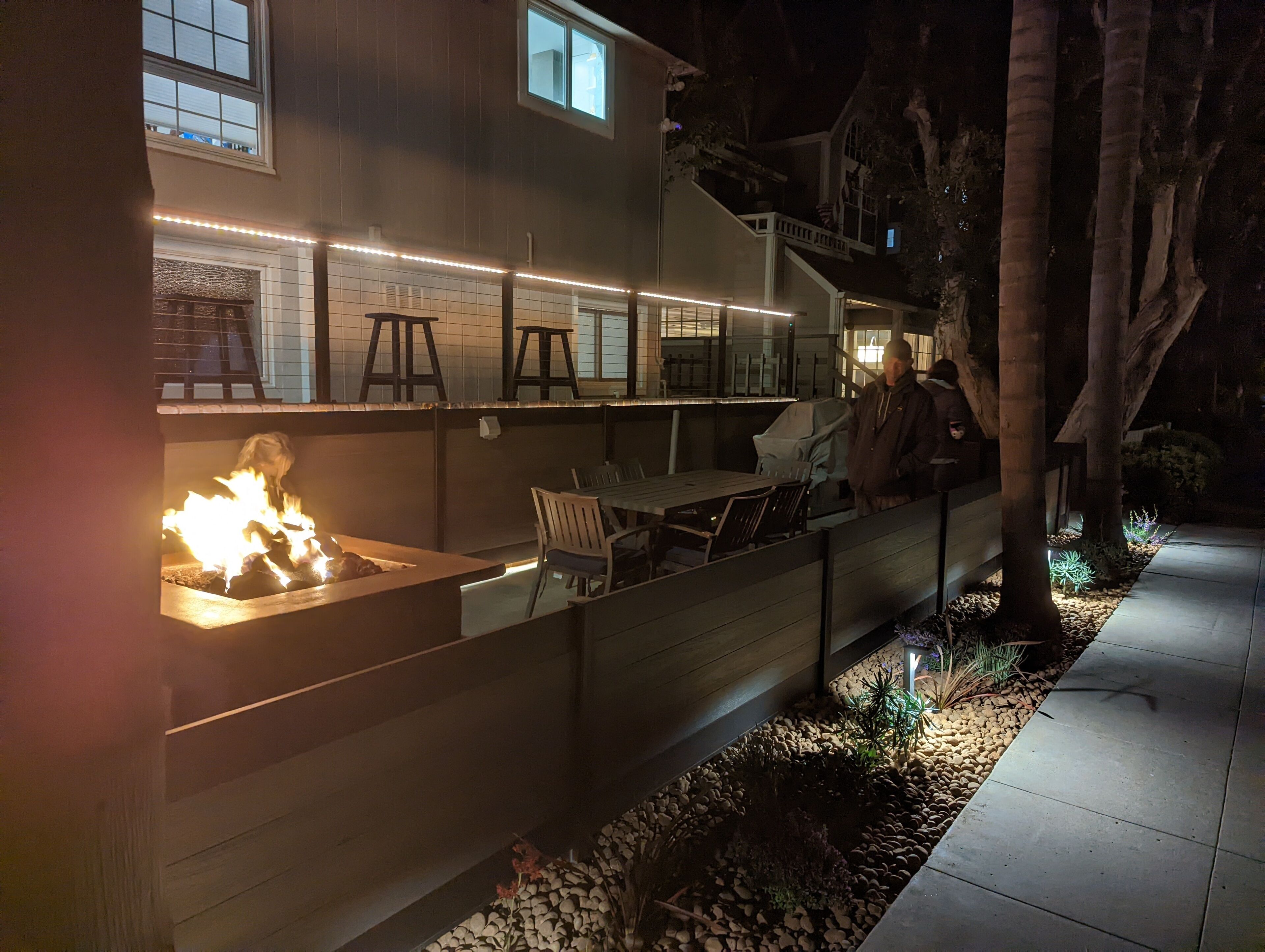 An outdoor patio area with a fire feature, seating, and a view of a house.