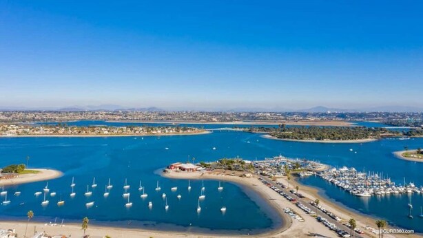 An aerial view of a marina with numerous boats docked, a sandy beach, and a cityscape in the background. - Seas the Day on the Bay (San Diego)
