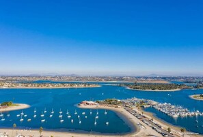 An aerial view of a marina with numerous boats docked, a sandy beach, and a cityscape in the background. - Seas the Day on the Bay (San Diego)