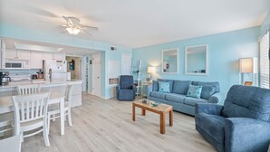 A modern living room with a blue sofa, a coffee table, and a dining area with white chairs. - Gulf View Beachfront Escape | Pool, Hot Tub & Pet-Friendly (Corpus Christi)