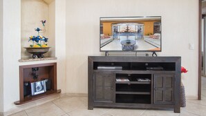 A living room with a flat-screen TV mounted on a dark wooden entertainment center, a decorative flower arrangement on a wall alcove, and a tiled floor. - Sonoran Sky 308 Must-see Clean Bright Ocean View Condo (Puerto Peñasco)