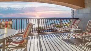 Un balcón con sillas a rayas y una mesa, con vista a una playa y al océano.