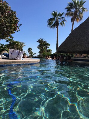 Une piscine aux eaux cristallines, bordée de palmiers, avec une structure à toit de chaume en arrière-plan.