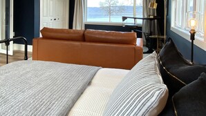 A modern bedroom with a large bed, a sofa, a desk, and a view of the outdoors. - Stunning 3 bed/3bath Renovated Cabin on Lake Pepin (Frontenac)