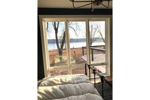 Enjoy a serene lake view from the comfort of your room, featuring a large window and a cozy bed with a comfortable headboard.