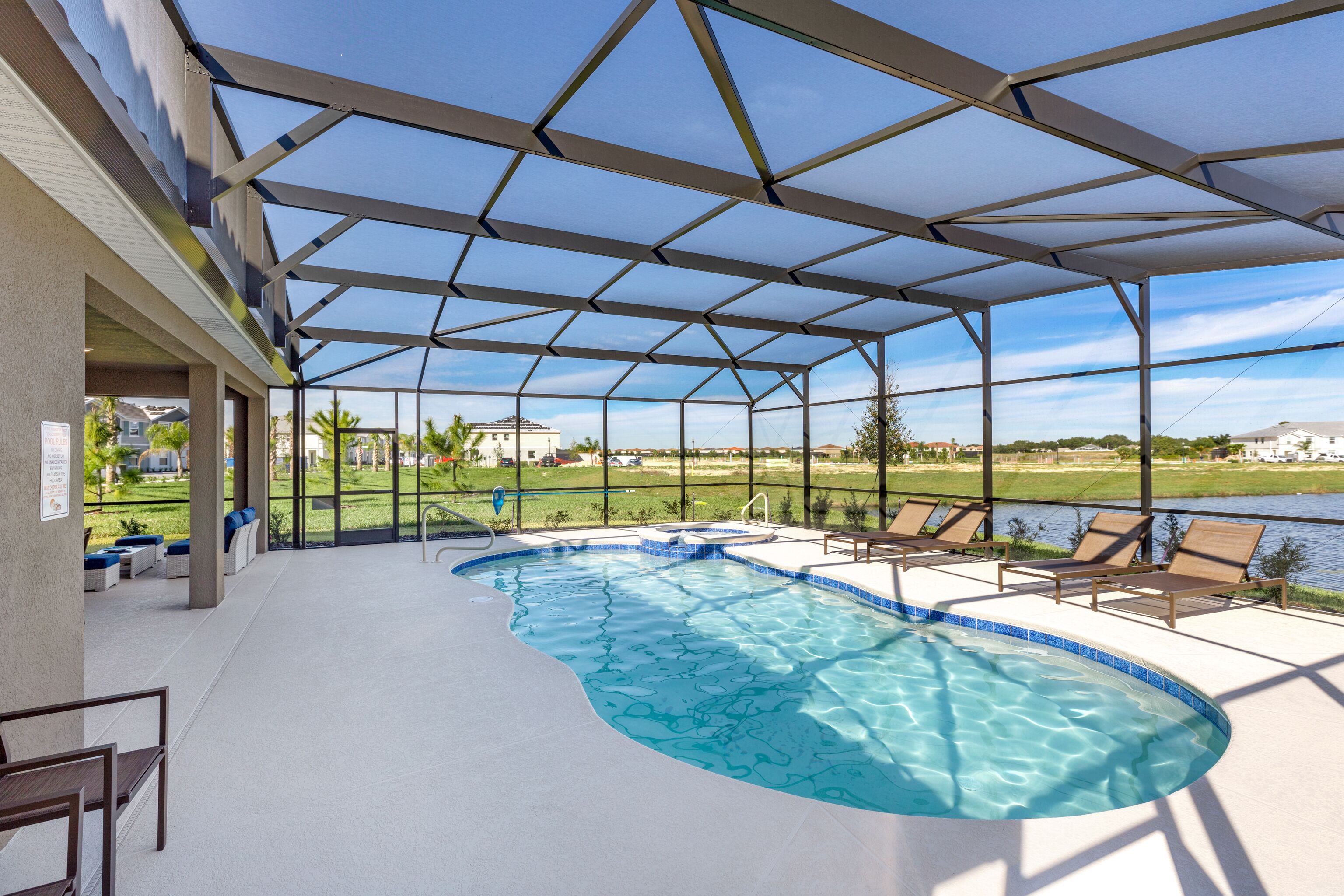 A covered swimming pool with clear blue water, surrounded by lounge chairs and a view of a golf course.