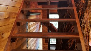 Una escalera de madera en una cabaña de troncos, con una ventana y parte del tronco de un árbol a la vista.