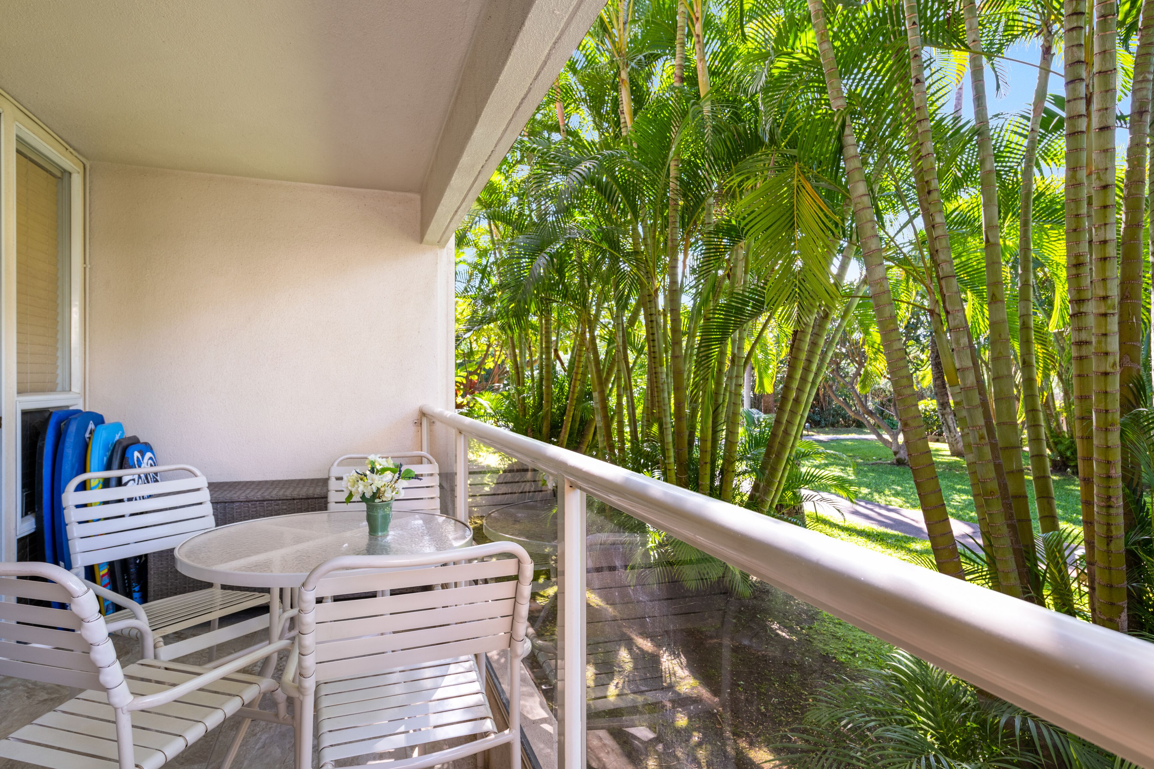 Uma varanda com mesa e cadeiras, dando vista para um jardim com palmeiras altas.