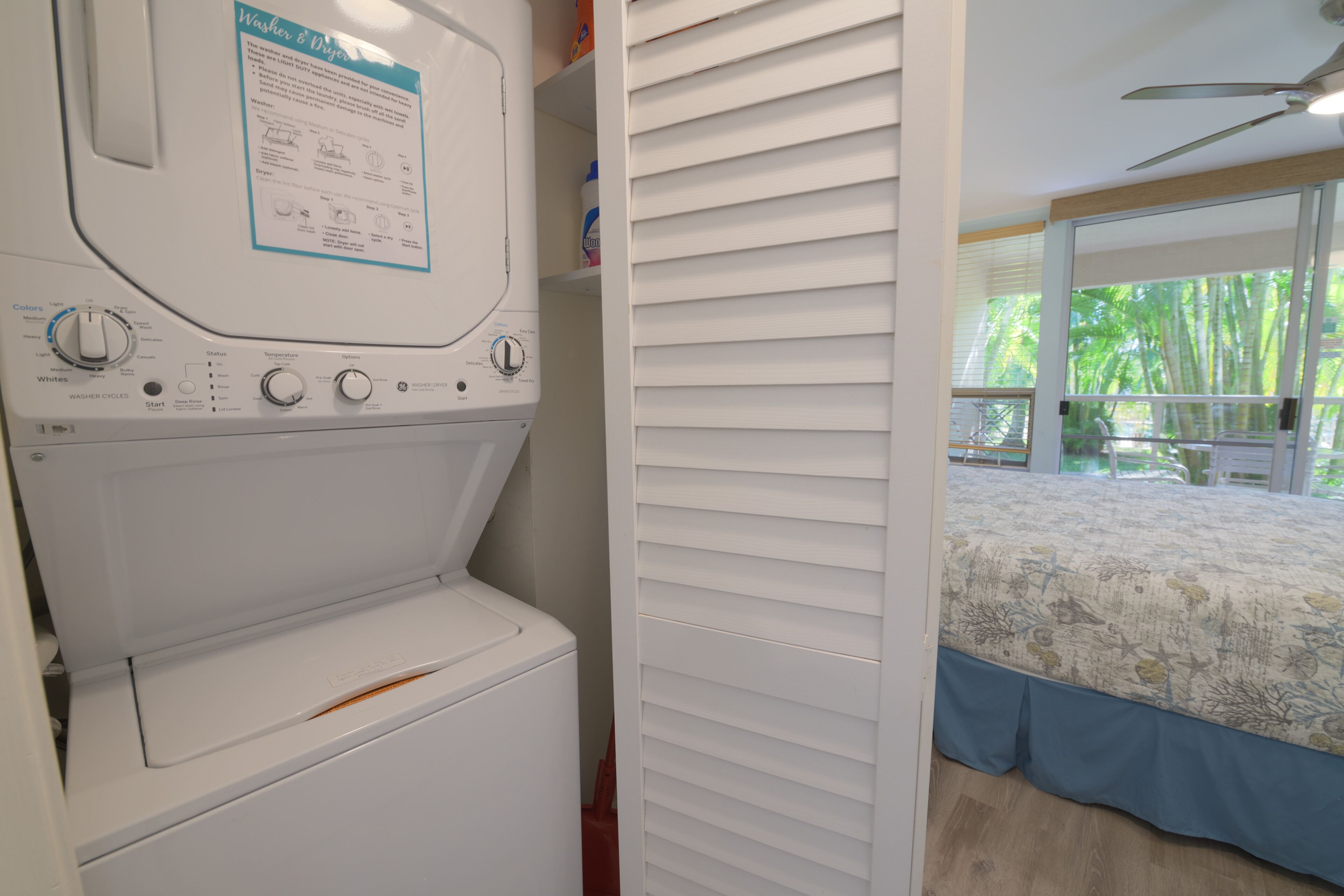 A laundry area with a front-loading washing machine and dryer, a control panel with various settings, and a window with a view of greenery outside.