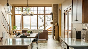 A modern kitchen with a large island, stainless steel appliances, and a view of a snowy landscape through large windows. - Newly built Mosier Bluff home-3 Bed, 3.5 Bath Spectacular River View and Hot Tub (Mosier)