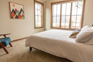 Ein Schlafzimmer mit einem großen Bett, einem blauen Sessel und Blick ins Freie durch ein Fenster.