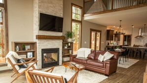 A spacious living room with a fireplace, leather sofa, wooden chairs, and a dining area with a kitchen in the background. - Newly built Mosier Bluff home-3 Bed, 3.5 Bath Spectacular River View and Hot Tub (Mosier)