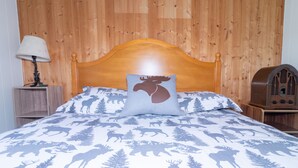 A bed with a moose-themed bedspread, a wooden headboard, a radio on a nightstand, and a lamp.