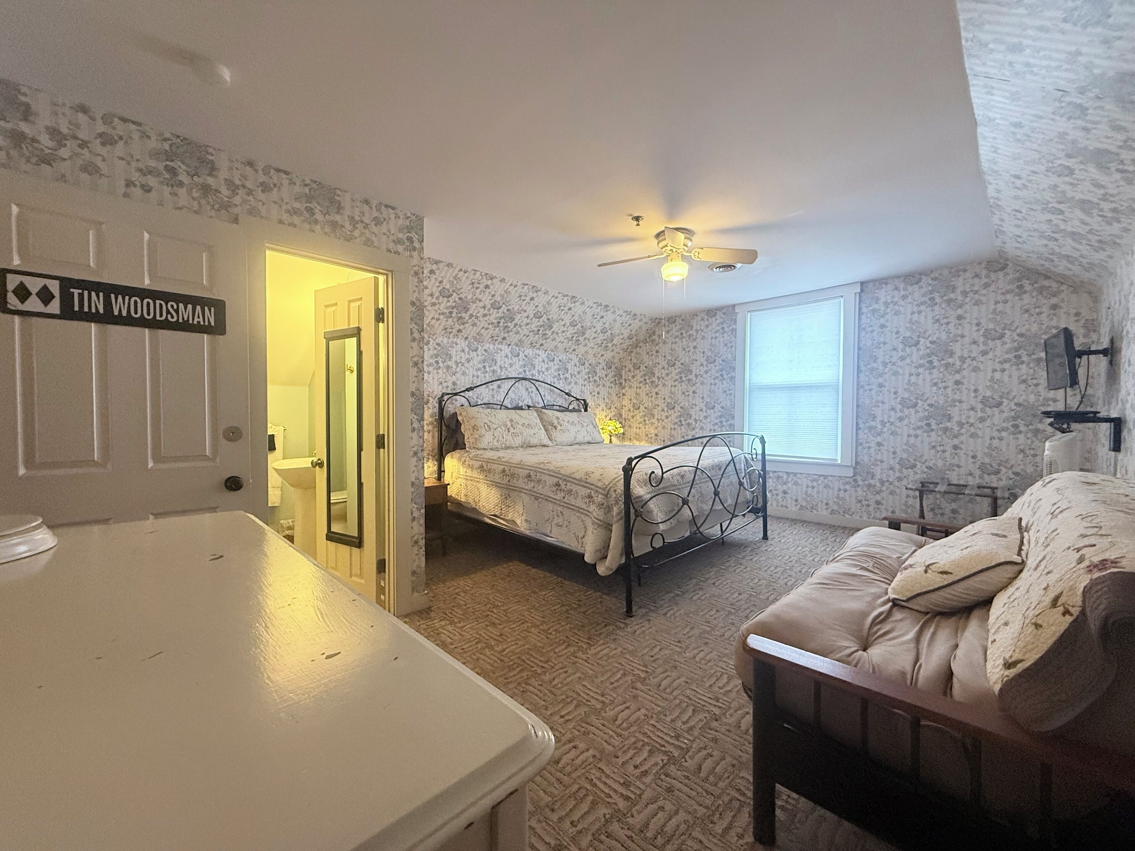 A bedroom with a bed, a chair, a desk, a ceiling fan, and a window.