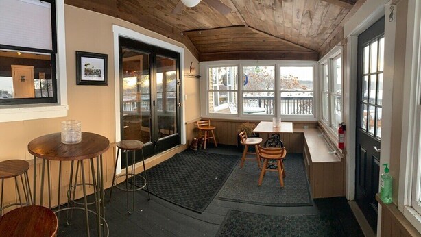A cozy room with a wooden ceiling, large windows, a small table, and a bench.