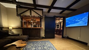 A cozy living room with a dark blue patterned rug, a wooden coffee table, a leather sofa, and a bar area with a wooden ceiling and exposed beams.
