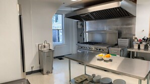 A commercial kitchen with stainless steel appliances, a large exhaust hood, and a variety of dishes and utensils on the counter.