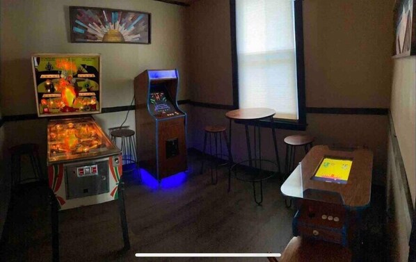 A room with a jukebox, a pinball machine, and a small bar area with stools.