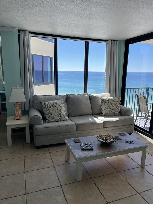A living room with a grey sofa, a coffee table, and a view of the ocean through large windows.