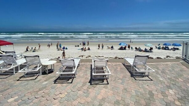 Un patio frente a la playa con sillones y sombrillas, con vista al océano.