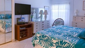 Un dormitorio con cama, televisor, escritorio, silla, cómoda y ventilador de techo.