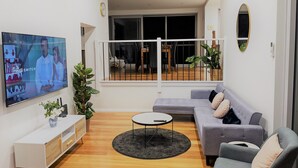 A modern living room with a flat-screen TV, a grey sofa, a small round coffee table, and a white console unit. - Brand new house, amazing views, walk to the beach! (Kiama)